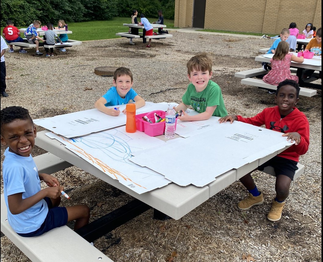 Four children drawing on large cardboard