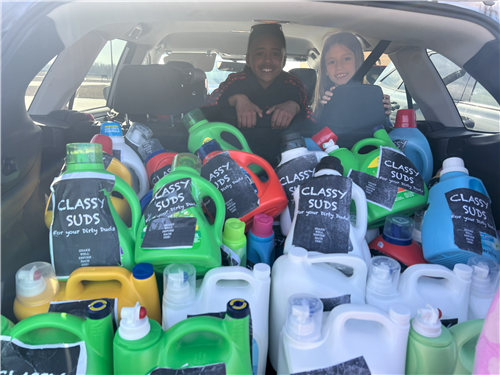 KIDS IN BACK OF CAR WITH MULTIPLE JUGS OF "CLASSY SUDS"