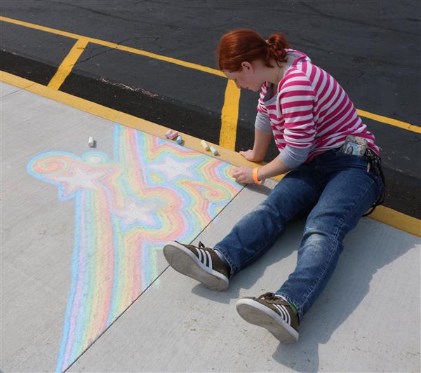 A student uses chalk to draw upon the sidewalk.